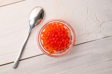 Red caviar in a glass jar with a spoon on a wooden table, macro, top view.