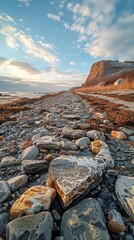 Picturesque coastal pathway of stone and gravel leading towards distant mountains during a serene sunset with a partly cloudy sky