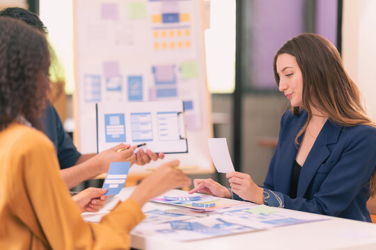 A team of UI UX web designers are working together to develop a mobile responsive website while discussing a project at a modern conference table. Brainstorming