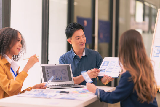 A team of UI UX web designers are working together to develop a mobile responsive website while discussing a project at a modern conference table. Brainstorming - Powered by Adobe