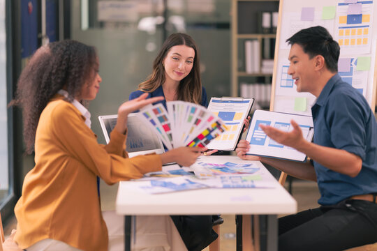 A team of UI UX web designers are working together to develop a mobile responsive website while discussing a project at a modern conference table. Brainstorming