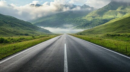 Smooth asphalt road leading to green, misty mountains with morning clouds overhead, evoking a peaceful drive.
