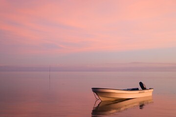 Small boat in front of a deep purple sky reflecting in the sea. Full purple sky with almost no horizon. Stunning evening sky just after sunset. Yasawa Islands tranquility. Invisible horizon. Fiji.  