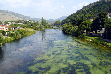 Fototapeta premium Landscape from Trebinje: view from the Arslanagic bridge to the Trebišnjica river, its green banks and mountains. Photo taken during a summer trip to the beautiful places of Bosnia and Herzegovina