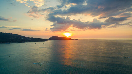 Naklejka premium A breathtaking aerial view of a coastal bay at sunset, with golden light reflecting on the calm sea and silhouetted hills in the distance. beautiful reflection of the golden sun at Patong Bay Phuket.