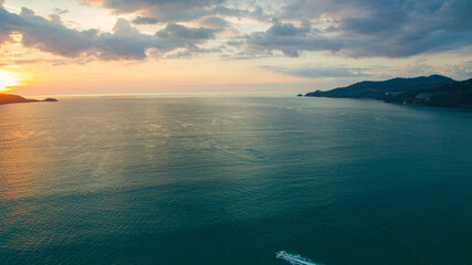 Fototapeta premium A breathtaking aerial view of a coastal bay at sunset, with golden light reflecting on the calm sea and silhouetted hills in the distance. beautiful reflection of the golden sun at Patong Bay Phuket.