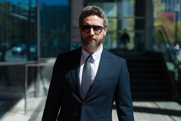 Fototapeta premium Confident business man standing outdoor on modern office building. Business success. Business man thinking outdoor. Modern businessman in full suit standing outdoors near office cityscape.