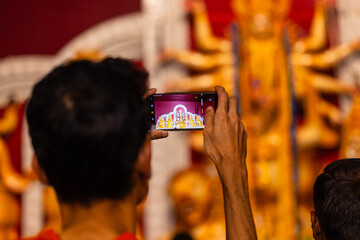 Shubho mahalaya, Hand holding mobile phone and taking photos of Goddess Durga idol at a pandal...