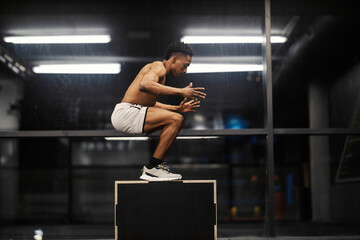 Naklejka premium Side view of active shirtless diverse sportsman jumping on jumping box at gym.