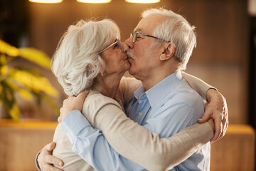 Romantic senior couple hugging and kissing at cozy home.