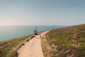 Caucasian casual attire man walking Whippet dog along clifftop coastal path towards Bedruthan Steps...