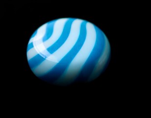 Obraz premium a close-up of a blue and white striped candy resting on a black background, emphasizing its round shape and shine create with ai
