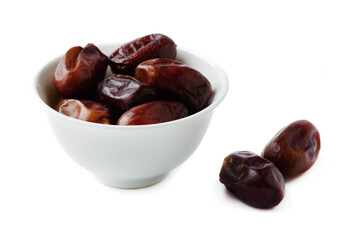 Dried dates in a white bowl and on a white background.