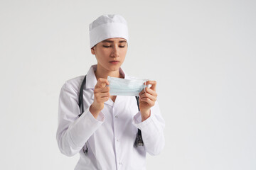 Portrait of young female doctor putting on protective medical face mask on white background, copy space