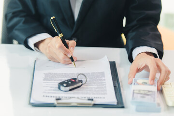 Car salesman signs car sales contract with cash and hands over keys to customer. Automotive business concept.