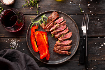 Grilled beef steak, well done with seasons and a glass of red wine on a black wooden background and plate top view