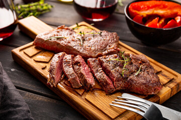 Grilled beef steak, well done with seasons and green on a black wooden background close up
