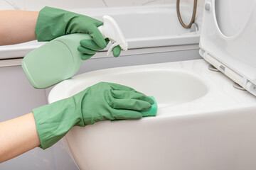 Woman in rubber gloves sprays cleaning agent on toilet bowl. Cleaning the toilet bowl