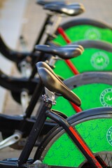 Obraz premium A collection of bicycles with bright green wheels sits neatly in a bike-sharing dock as the evening sun casts a warm glow, inviting riders to explore the city
