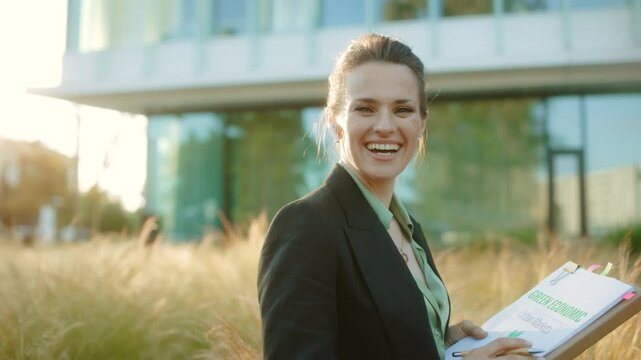smiling modern 40 years old woman employee near business center in black jacket with documents and folder.