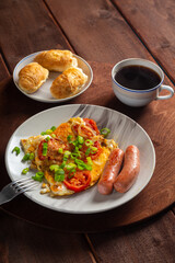 Eggs with tomatoes and sausages in a plate on a wooden table of coffee and croissants on a round stand