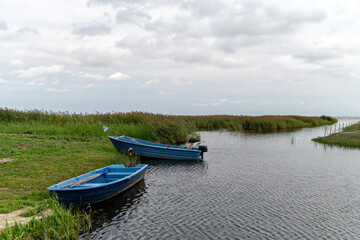 Calm waters with blue boats moored along a serene riverbank during a cloudy afternoon