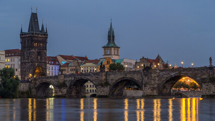 The Charles Bridge day to night timelapse over the Vltava River reflected in water in Prague, Czech Republic