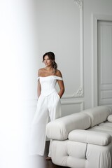 Elegant middle-aged woman in white suit posing in light interior of photo studio