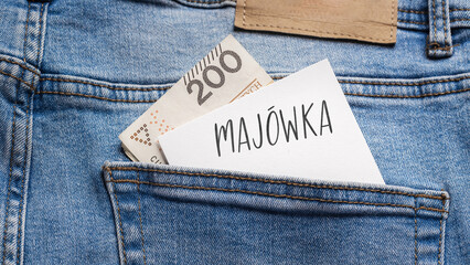 White card with a handwritten inscription "MAJ&Oacute;WKA", put into the pocket of blue pants jeasnow, next to Polish banknotes PLN (selective focus), translation: MAY DAY