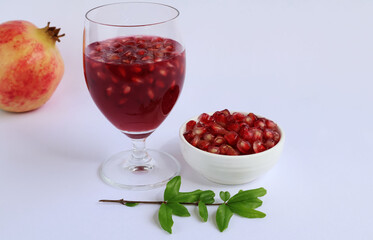 Red juice with pulp gathered together in a glass and in a cup. Next is the Punica granatum fruit, with the leaves at the front on a white background.

