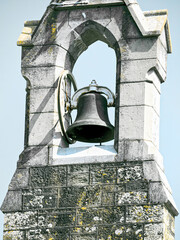 Obraz premium A bell is mounted on a stone tower. The bell is made of metal and has a circular frame. The tower is made of light-colored stone with visible wear and tear.