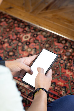 Holding smartphone, person browsing on blank screen over patterned rug, copy space