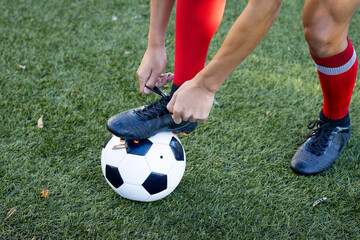 Tying shoelaces on soccer field, player preparing for football match