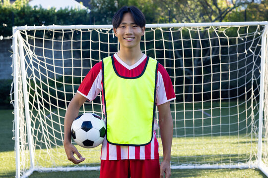Smiling teenage male soccer player holding ball and standing in front of goal on field