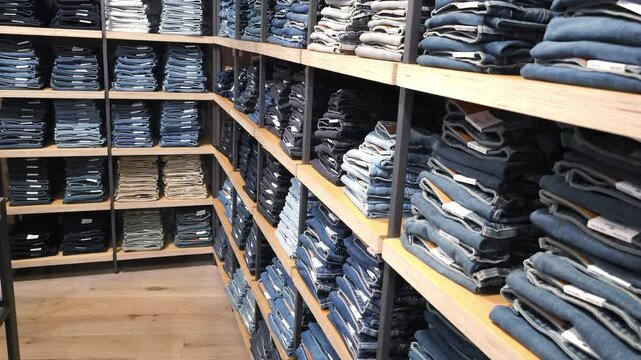Stacks of folded denim jeans on wooden shelves in a retail store. Organized clothing display and retail merchandising concept.