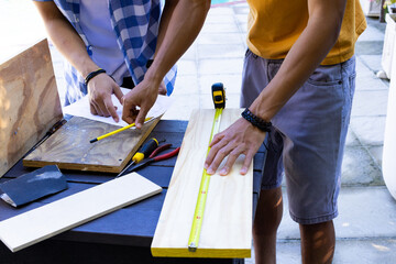 Measuring and marking wood, Asian father and teenage son working on carpentry project outdoors