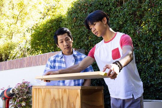 Measuring wooden plank, Asian father and teenage son working on DIY project outdoors