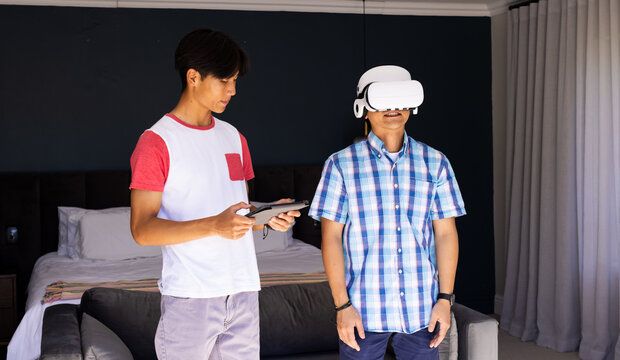Using vr headset, asian father and teenage son holding tablet in bedroom