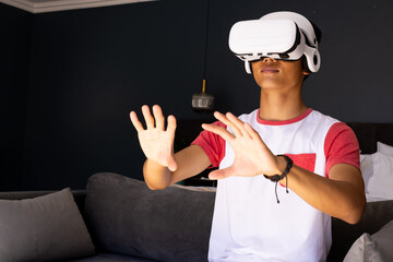 Using VR headset, young asian man interacting with virtual environment in living room, copy space
