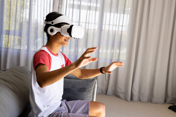 Using VR headset, young asian man interacting with virtual environment in living room, copy space