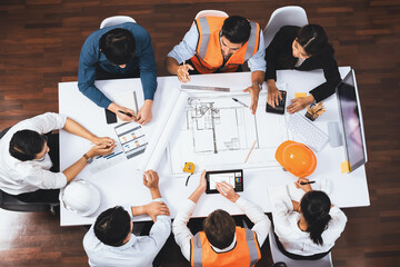 Top view banner of diverse group of civil engineer and client working together on architectural project, reviewing construction plan and building blueprint at meeting table. Prudent