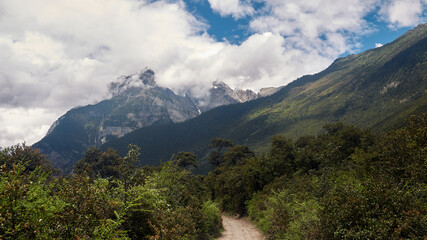 path in the woods with mountains covered by cloud in eastern tibet