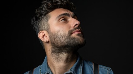 Fototapeta premium Portrait of young man with curly hair and beard wearing retro shirt and suspenders showing serious expression and stylish confidence against black background.