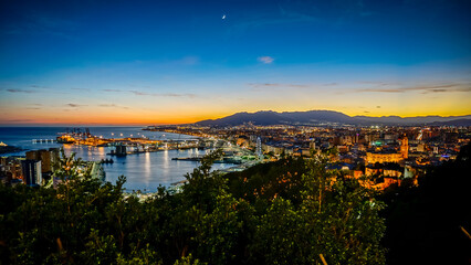Fototapeta premium Panoramic view of Malaga city at sunset with the port in the foreground and the mountains in the background
