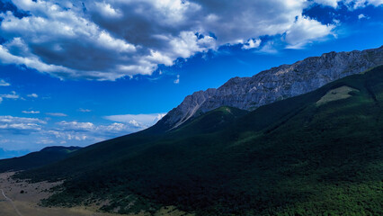 Green mountain landscape with rocky cliffs under blue sky with clouds