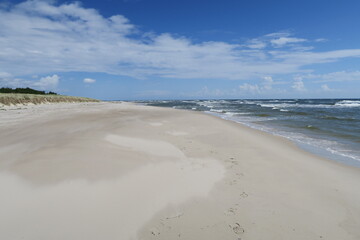 Wellen branden am Strand Sandhammaren in Ystad in der schwedischen Region Skane. Im Hintergrund sind weiße Schleierwolken zu sehen. Den Strand begrenzen Sanddünen mit Bewuchs. 