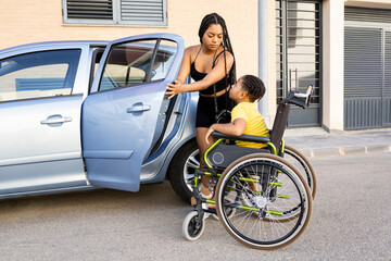A young black woman with braids helps her little brother who is in a wheelchair into the car....