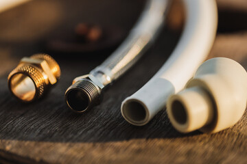 Plumbing parts lying on a rustic wooden table on a sunny day. PEX pipe, hose and brass nipple (selective focus)