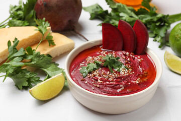 Tasty beetroot hummus in bowl and products on white table