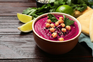 Tasty beetroot hummus in bowl and products on wooden table, closeup